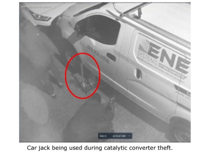 Still image of surveillance footage showing masked man stealing catalytic converter from a van. 