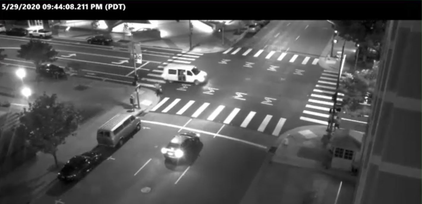 A picture of a four-way intersection at night with cars and trees lining the road.