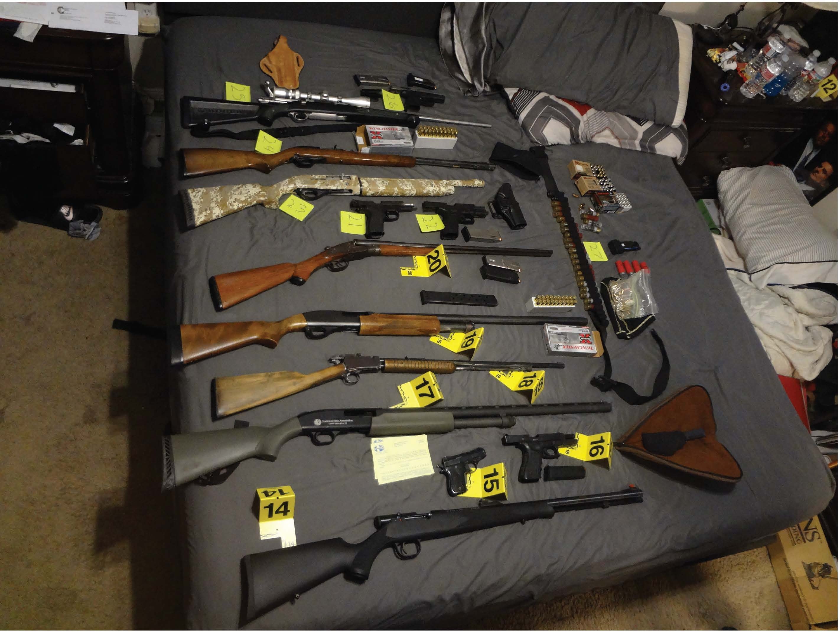 Thirteen firearms on a bed