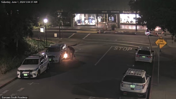 Early morning street scene with several parked cars and a figure setting fire to something under a car