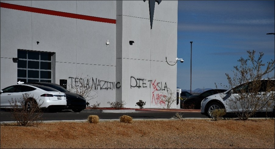 TESLA NAZI INC and DIE TESLA spray-painted in black and red on the façade of a white building.