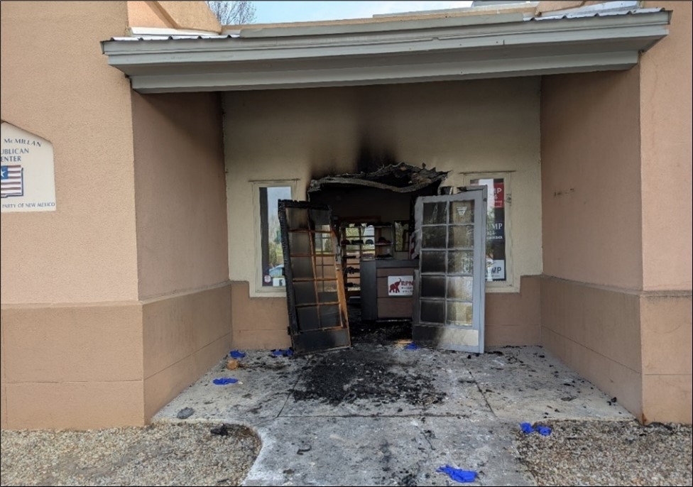 Depicts sustained fire damage to the exterior door of a brown building. 